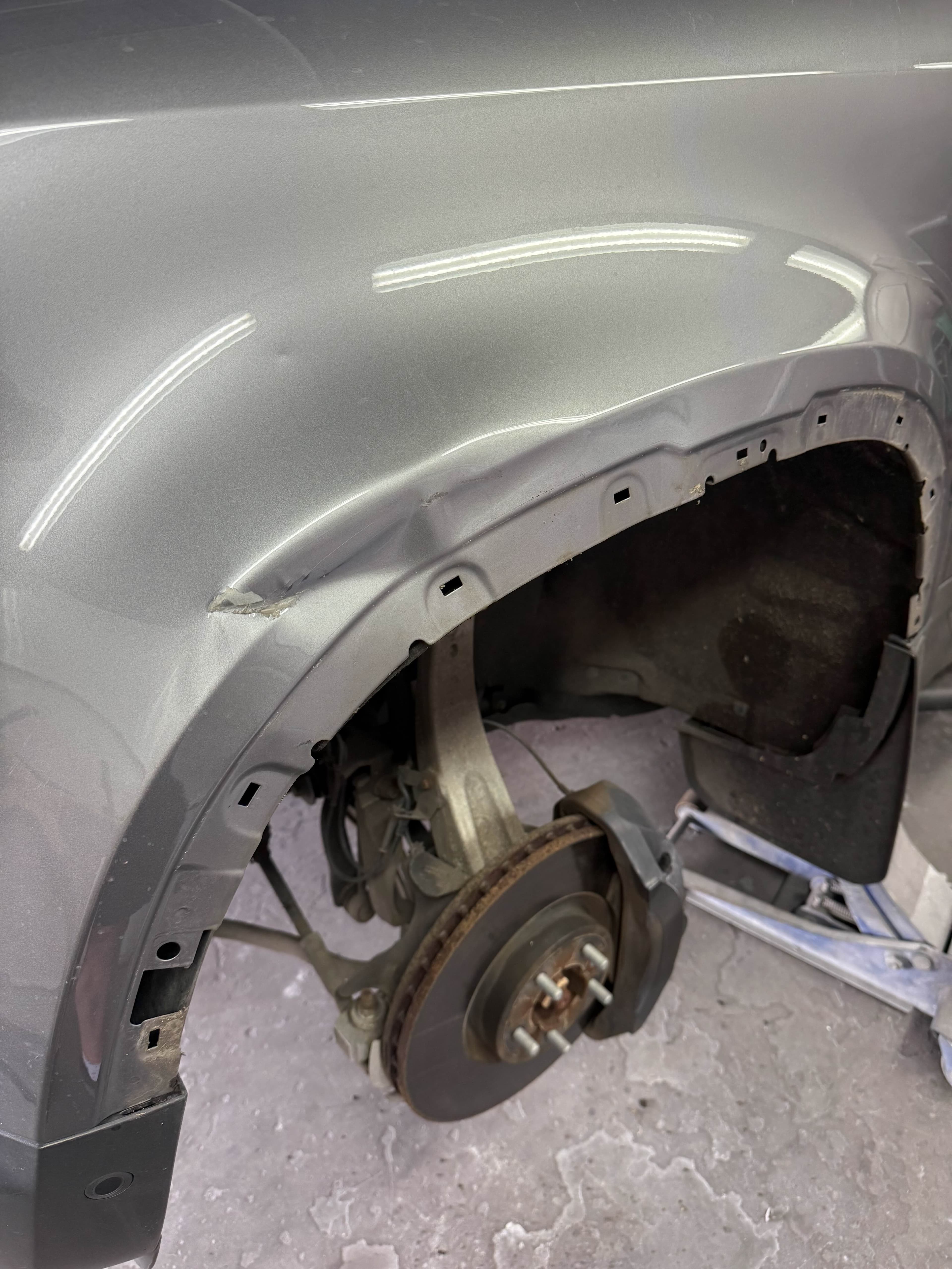 Damaged grey front wing around the wheel arch before repair